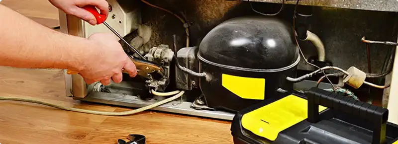 Refrigerator repair technician fixing the compressor and wiring in Lakewood, CA