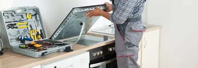 Cooktop repair technician lifting a built-in stovetop for service in Long Beach, CA