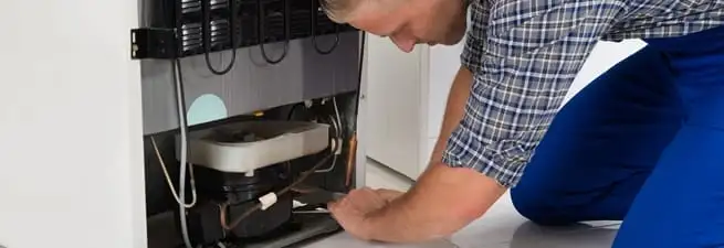 Refrigerator repair technician servicing the compressor and condenser area in Long Beach, CA