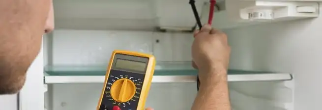 Refrigerator repair technician testing electrical components with a multimeter in Long Beach, CA
